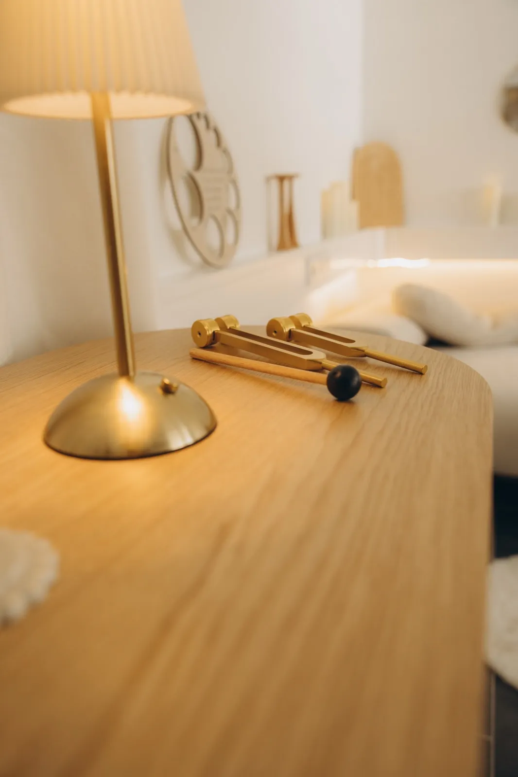 Detail aus dem AVORA Women's Space: goldene Lampe und Klanggabeln auf einer Holzkommode im warmen Licht