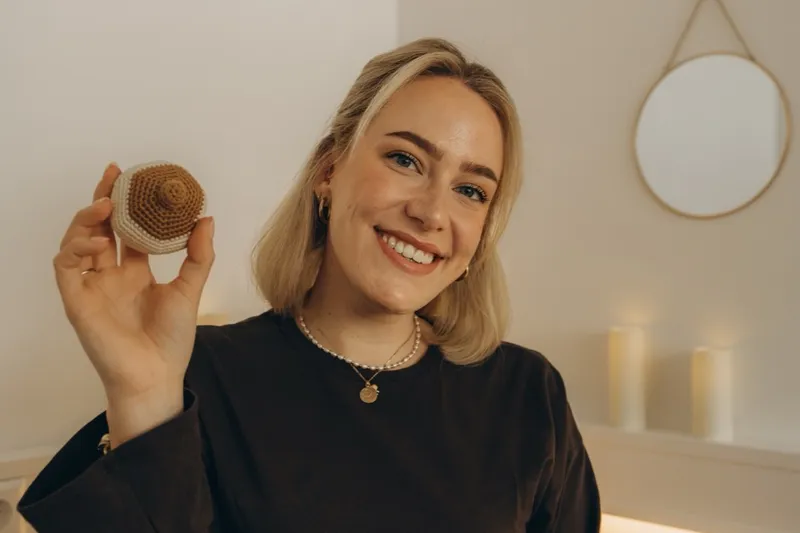 Verena Radke lächelt in die Kamera, in der Hand ein gehäkeltes Brust-Modell für die Stillberatung