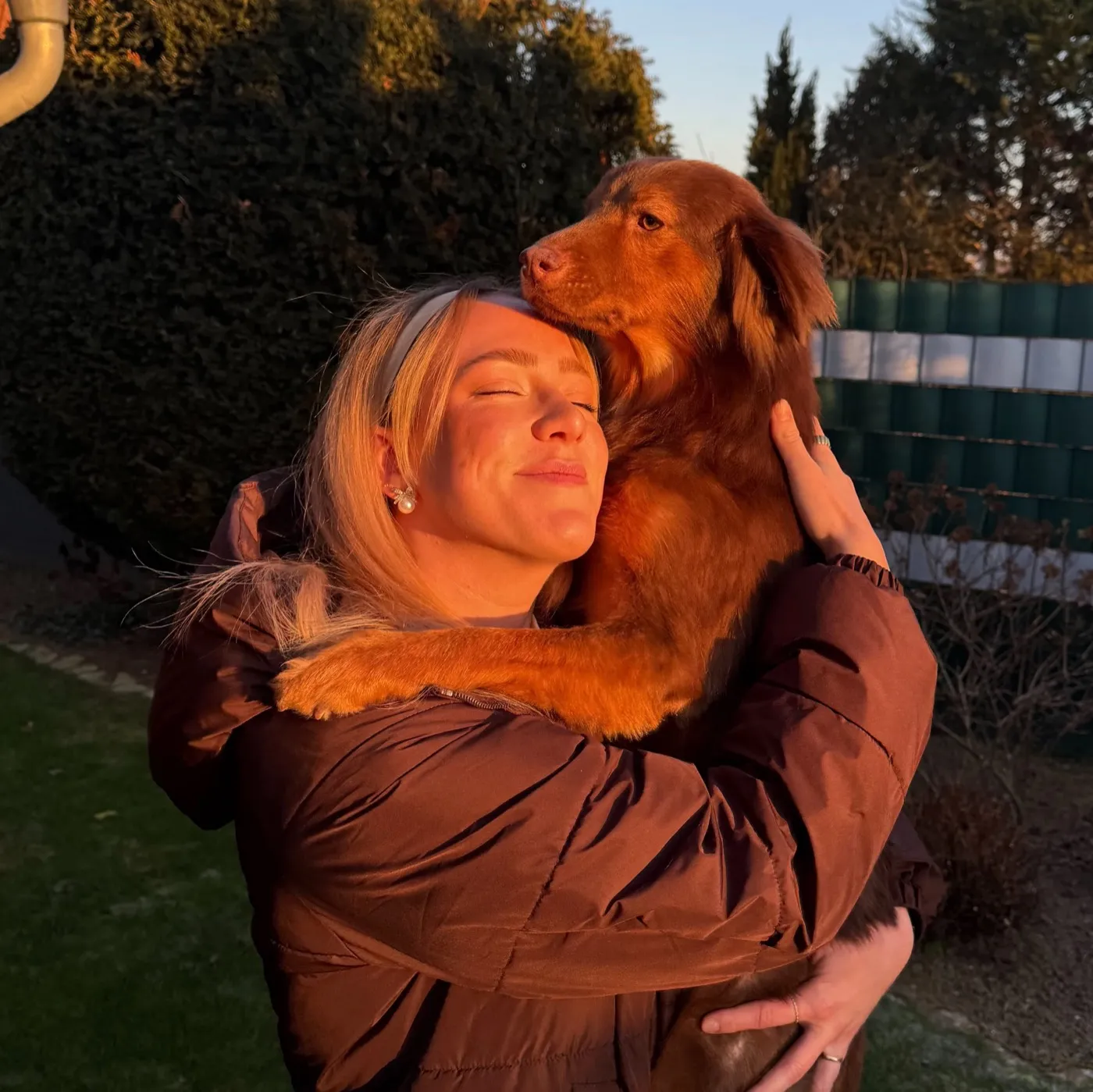 Verena privat: Sie umarmt ihren Hund im warmen Abendlicht im Garten