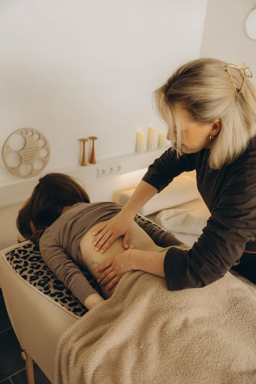 Verena massiert den Rücken einer Frau auf der Massageliege im warmen Kerzenlicht