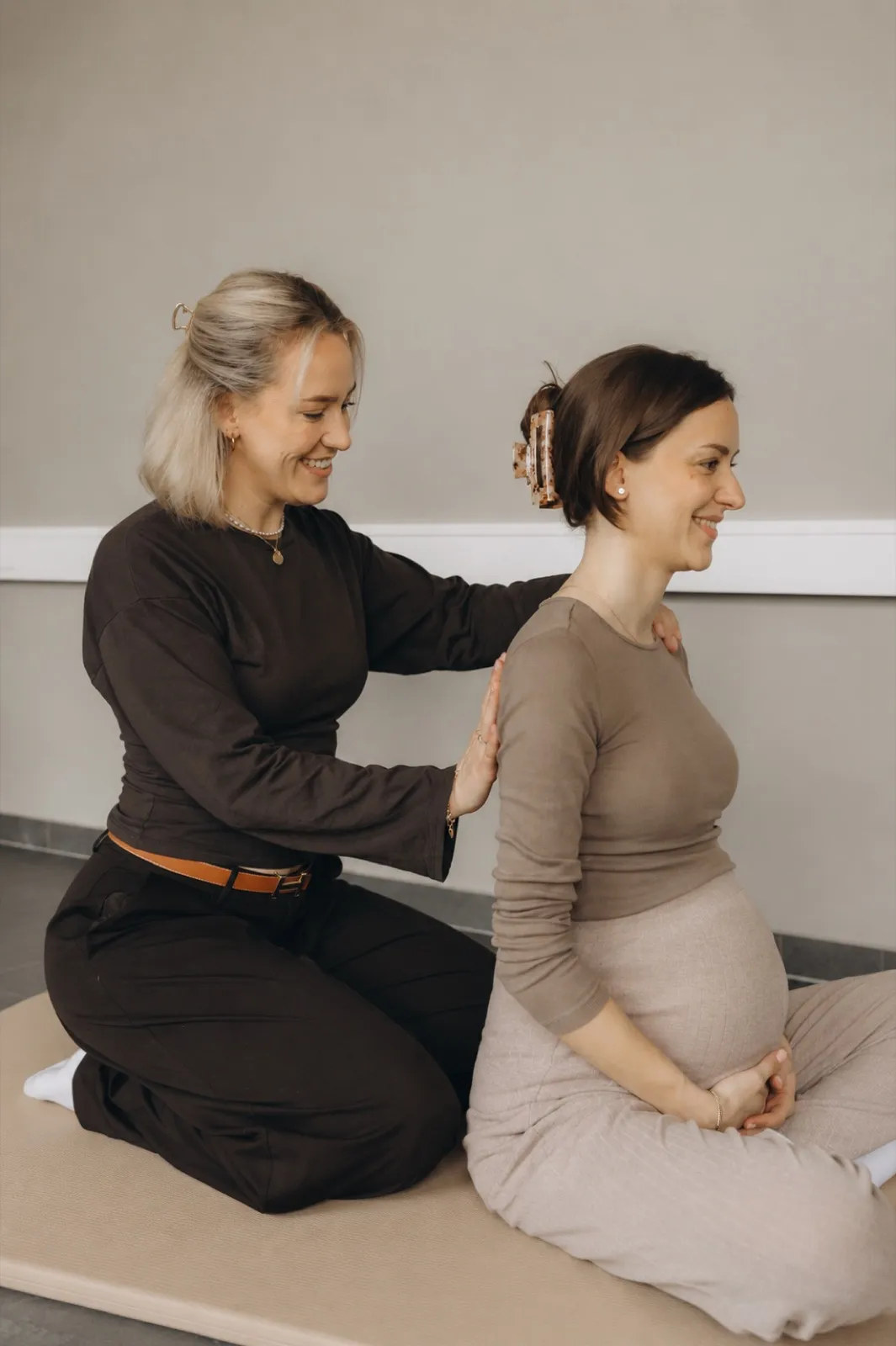 Verena unterstützt eine Schwangere bei einer aufrechten Haltung auf der Yogamatte